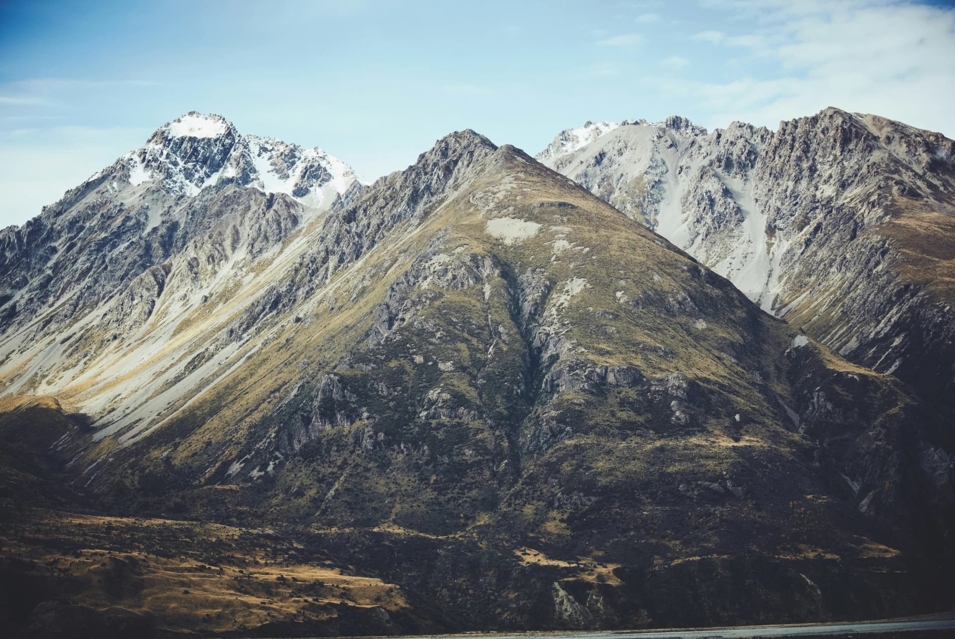 Rugged mountain range with snow-dusted peaks and grassy slopes under a pale blue sky